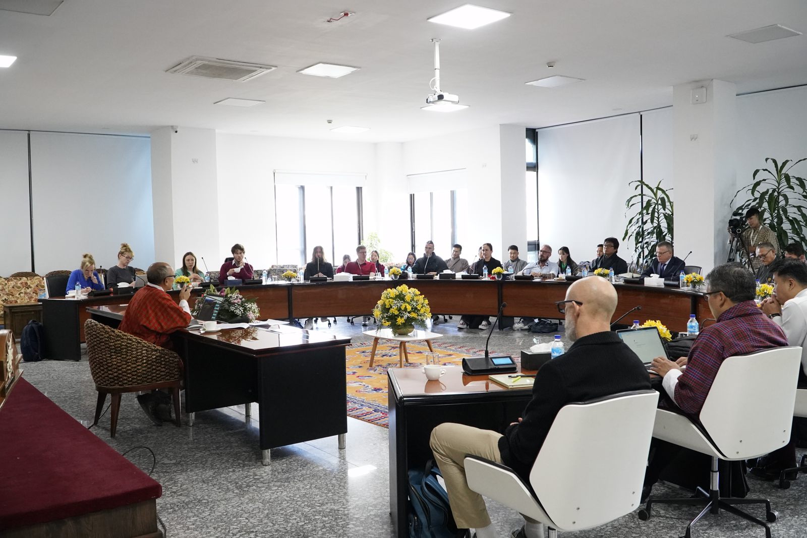 Scholars and Bhutanese hosts seated around a large open square of tables during a forum session